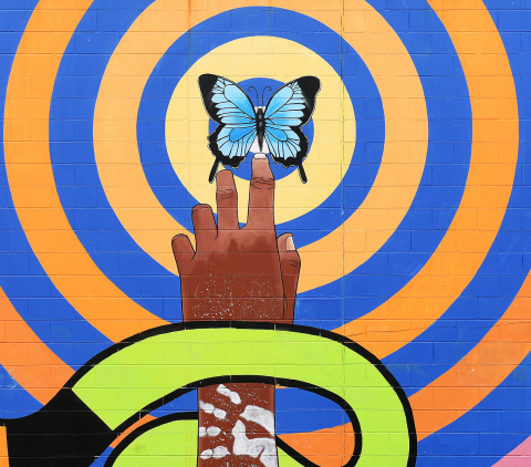 First Nations mural with hand reaching up to a blue butterfly with blue and orange circles encircling 