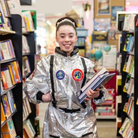 Girl in spacesuit costume holding books at QBD Books. 