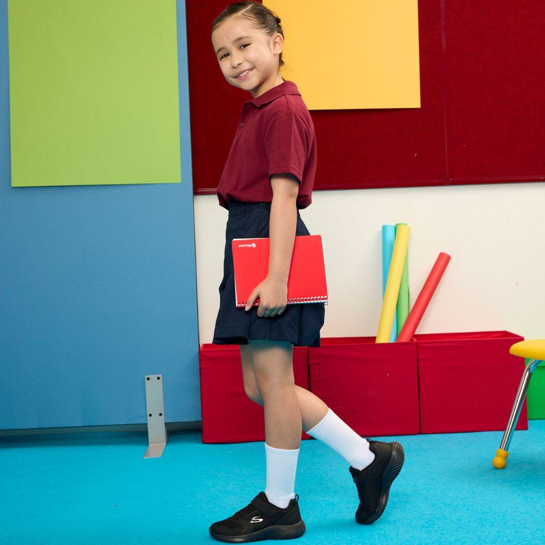 Girl in school uniform wearing Skechers school shoes.